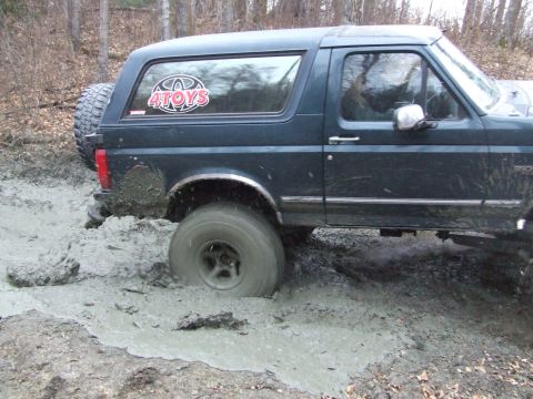 1990 Ford Bronco - This Ford Bronco is deep in the mud, with its tires struggling to find traction.