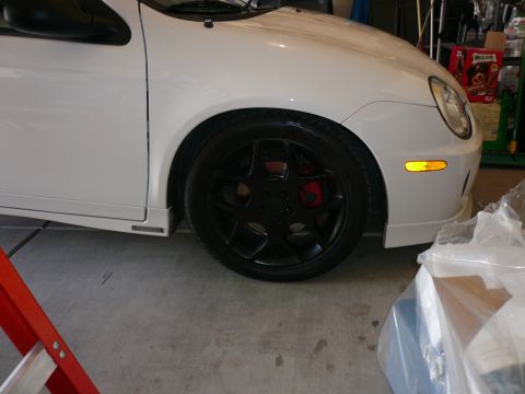 1996 Ford Probe - Close-up view of a white car's front wheel assembly, black rims and red brake calipers.