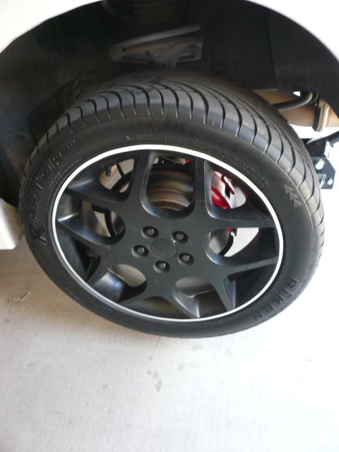 1996 Ford Probe - A close-up view of a car's wheel and tire assembly, showing a black five-spoke rim with a white accent ring.