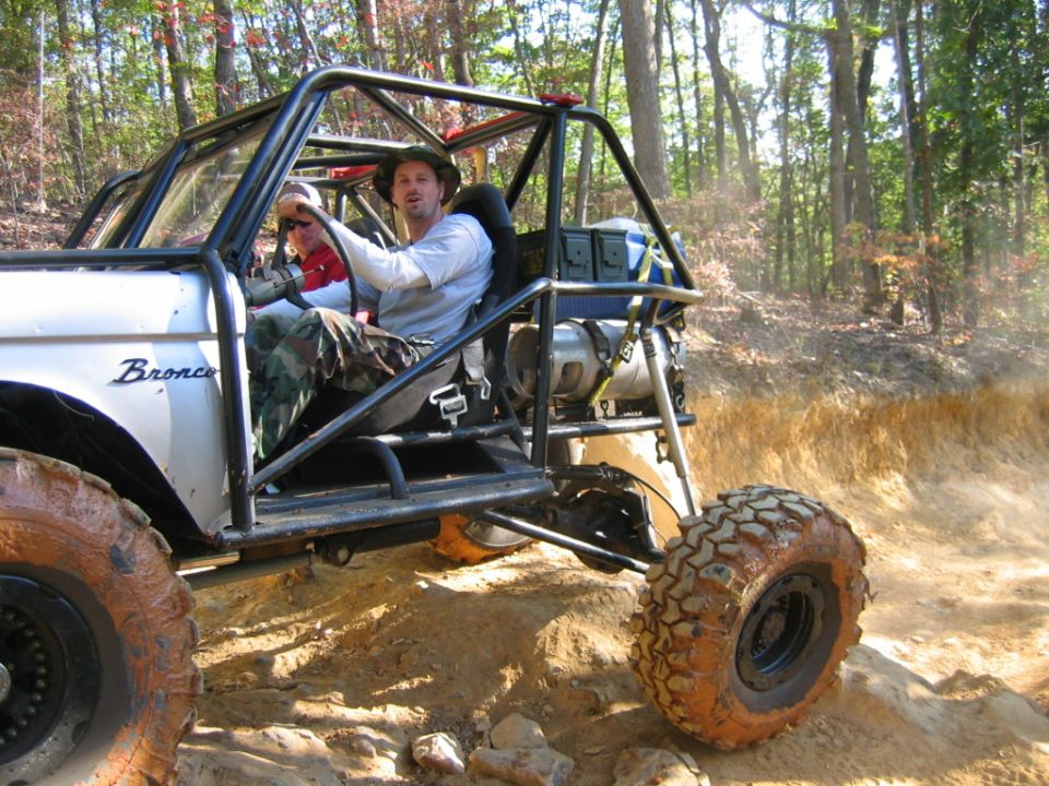 Off-road buggy with roll cage and two people inside, driving on a dirt trail