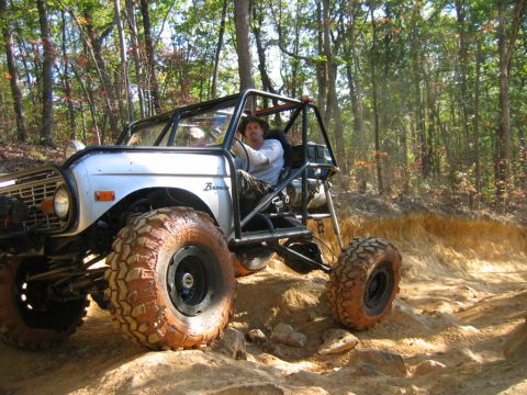 1992 Ford Mustang - A man drives a heavily modified off-road vehicle through a wooded trail with sandy terrain.