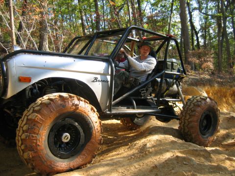 1992 Ford Mustang - A man drives a modified off-road vehicle through a wooded area on a dirt path.