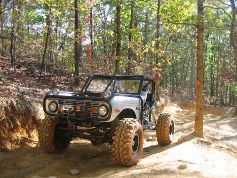 1992 Ford Mustang - Modified off-road vehicle navigates a wooded trail with large, aggressive tires.