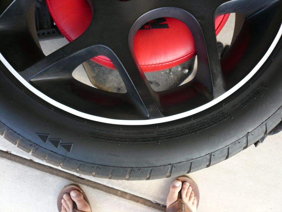 Black multi-spoke wheel with a white stripe and tire, red brake caliper visible behind spokes