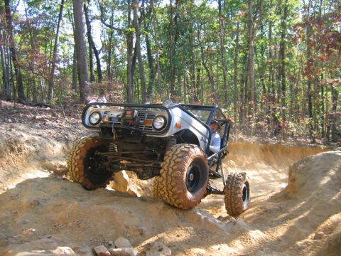 1992 Ford Mustang - A modified off-road vehicle tackles a challenging dirt path in a wooded area.