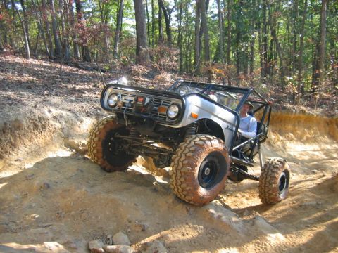 1992 Ford Mustang - Off-road vehicle with large tires navigates a challenging dirt trail in a wooded area.