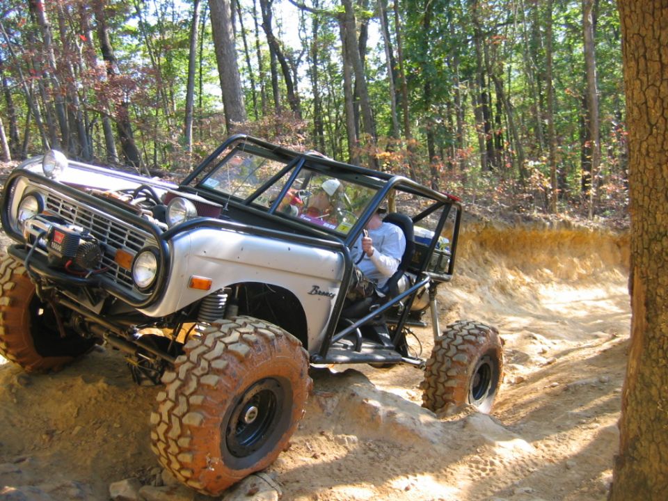 Off-road vehicle with a roll cage driving on a dirt trail. The vehicle has large tires and a winch on the front