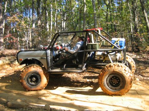 1992 Ford Mustang - Off-road vehicle modified with a roll cage and large tires navigates a dirt trail in a wooded area.