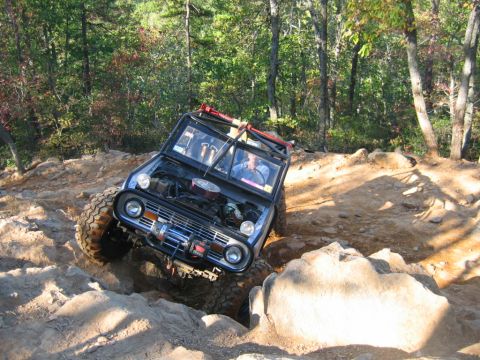 1992 Ford Mustang - An off-road vehicle navigates a challenging rocky trail with trees in the background.