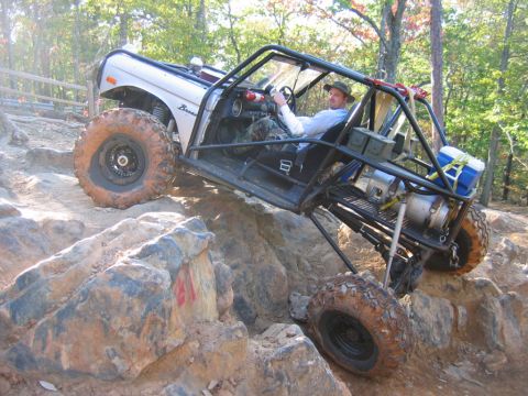 1992 Ford Mustang - A heavily modified off-road vehicle navigates a rocky trail, its extreme suspension and large tires.