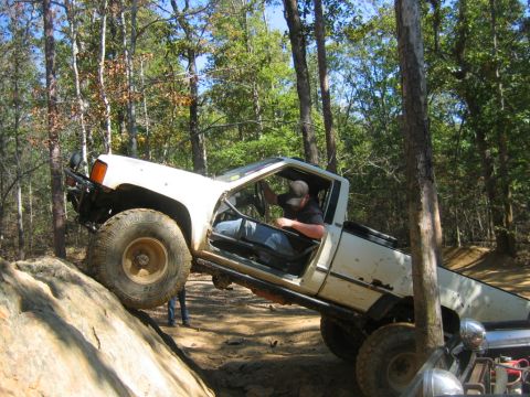 1992 Ford Mustang - A white pickup truck navigates a challenging off-road course, with one wheel high on a rock formation.