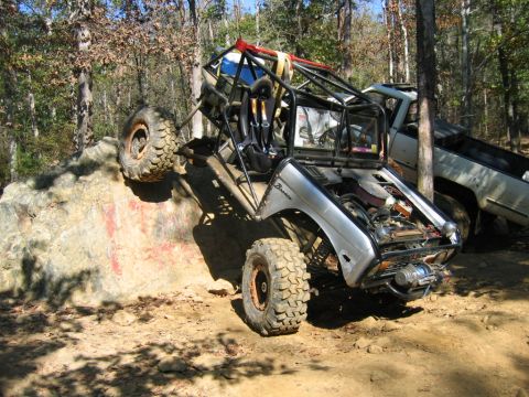 1992 Ford Mustang - Modified off-road buggy with a roll cage navigates a rocky terrain next to a pickup truck.