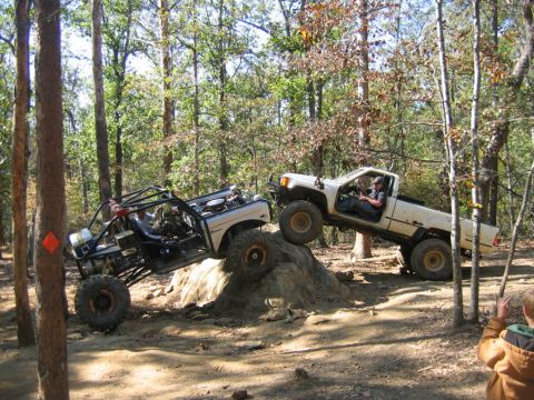 1992 Ford Mustang - Off-road trucks tackle a challenging rocky terrain in a wooded area.