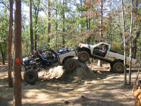 1992 Ford Mustang - Two off-road vehicles navigate a rocky obstacle on a wooded trail, demonstrating their climbing capabilities.