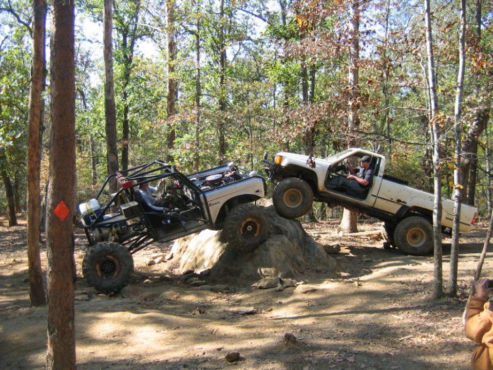 Off-road buggy and white pickup truck climbing rocks on a wooded trail