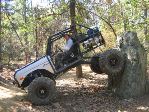 1992 Ford Mustang - Off-road vehicle with roll cage navigating a rocky trail in a wooded area.