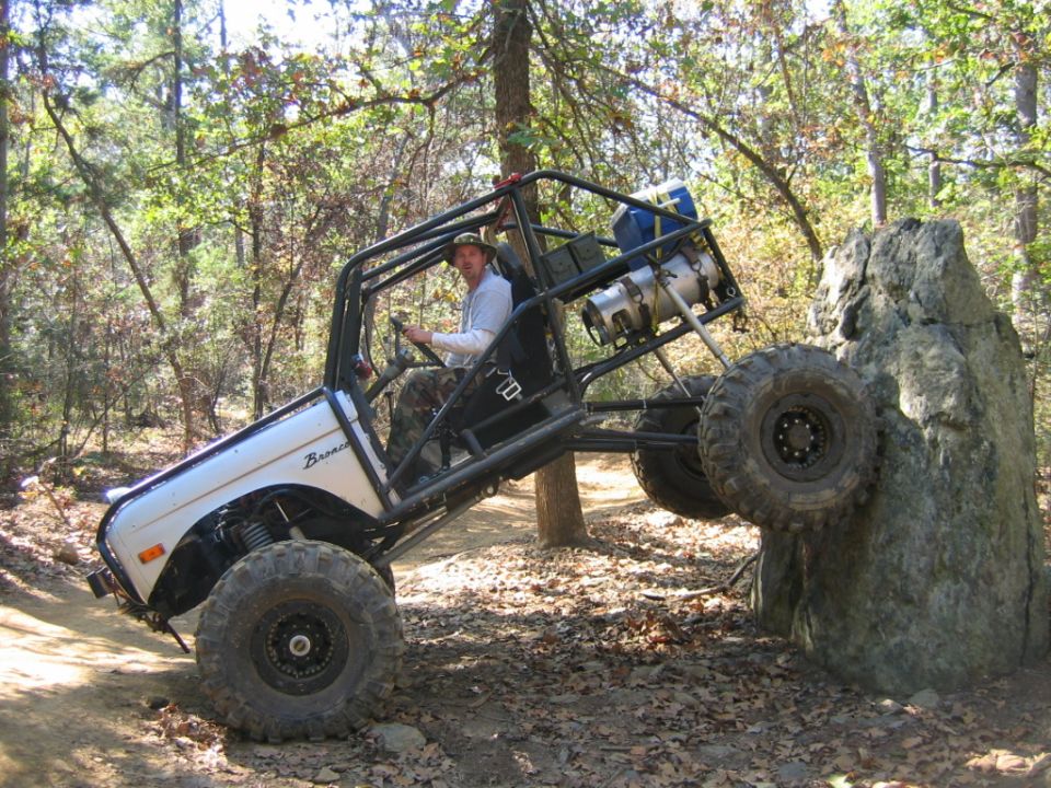 Modified off-road vehicle with roll cage climbing a large rock on a dirt trail