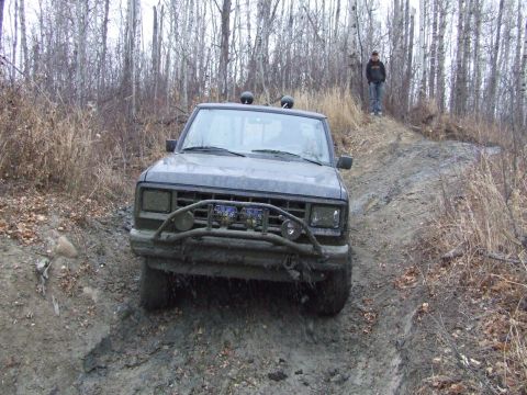1990 Ford Bronco - A person stands on a ridge as a mud-covered Ford Ranger navigates a difficult off-road trail.