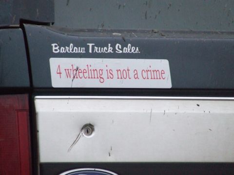 1990 Ford Bronco - A vehicle's rear gate displays stickers from Barlow Truck Sales and a message about off-roading.