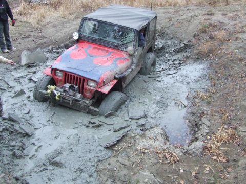 1990 Ford Bronco - A red Jeep Wrangler with flame decals on the hood is stuck in deep mud, with two people nearby.