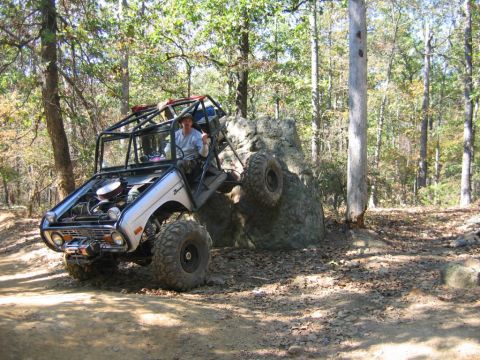 1992 Ford Mustang - A modified off-road vehicle navigates a rocky trail in a wooded area.