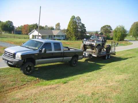 1992 Ford Mustang - Ford F-250 truck hauls a heavily modified off-road vehicle on a trailer through a rural landscape.