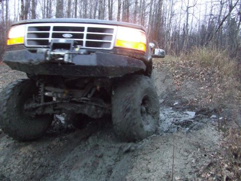 1990 Ford Bronco - This Ford Bronco is navigating a muddy trail in a wooded area.