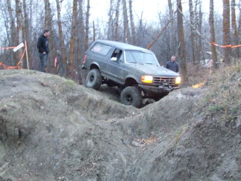 1990 Ford Bronco - 1990 Ford Bronco navigates a challenging off-road course in a wooded area.