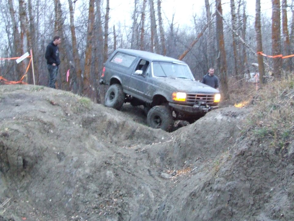 1990 Ford Bronco climbing a steep dirt incline with two people watching