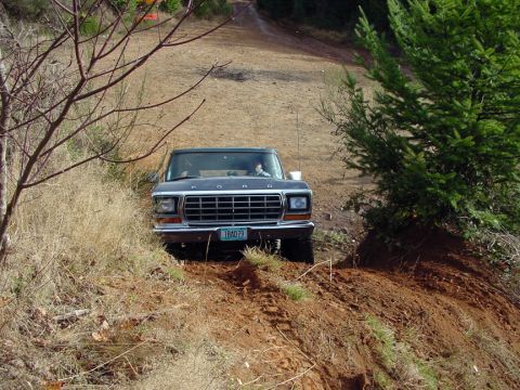 1979 Ford Bronco - A dark blue 1979 Ford Bronco navigates a dirt path, with a driver visible behind the wheel.