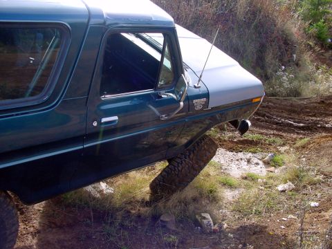 1979 Ford Bronco - A green Ford Bronco with a light blue hood is shown at an angle, with its front passenger wheel elevated off the ground.