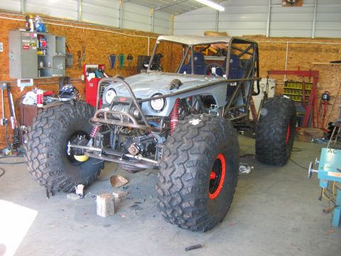 1992 Ford Mustang - Custom off-road buggy with oversized tires and roll cage, seen in a workshop setting.