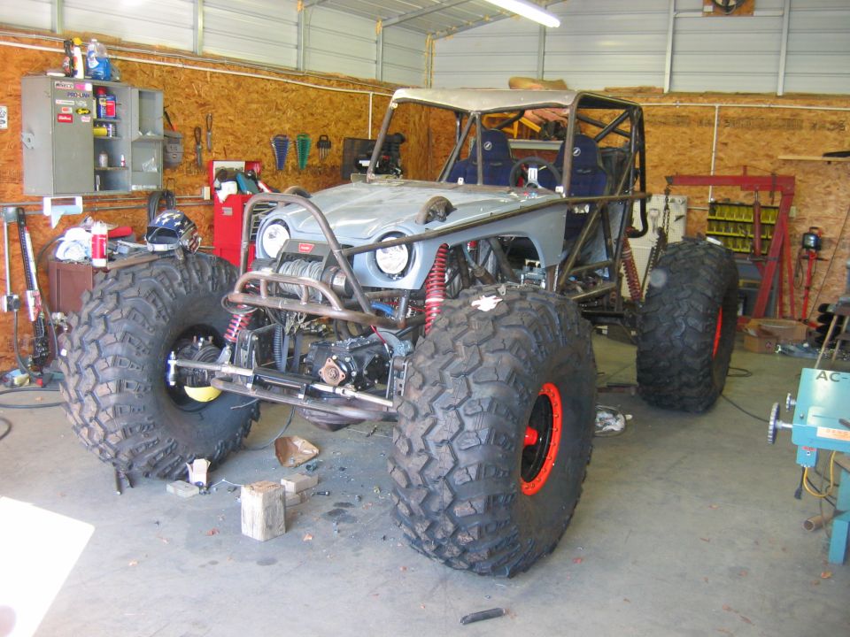 Custom off-road buggy with large tires, roll cage, and exposed engine components in a garage