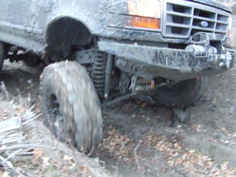 1990 Ford Bronco - A heavily muddied 1992 Ford Bronco navigates a rough, off-road terrain.