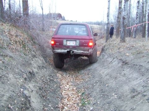 1990 Ford Bronco - Red SUV navigates a challenging off-road trail with steep banks and fallen leaves.