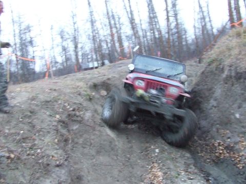 1990 Ford Bronco - A red Jeep Wrangler navigates a steep, muddy incline during an off-road excursion.