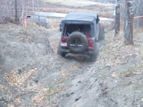 1990 Ford Bronco - A red Jeep Wrangler navigates a muddy off-road trail with another vehicle visible in the background.