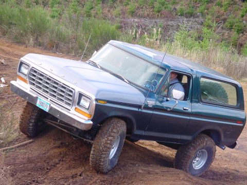 1979 Ford Bronco - 1979 Ford Bronco navigates an off-road trail with a driver at the wheel.