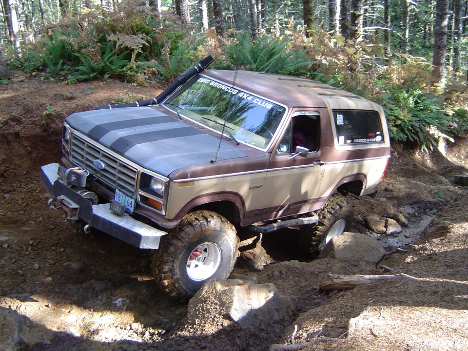 Two-tone brown lifted Ford Bronco crawling over a muddy rocky obstacle