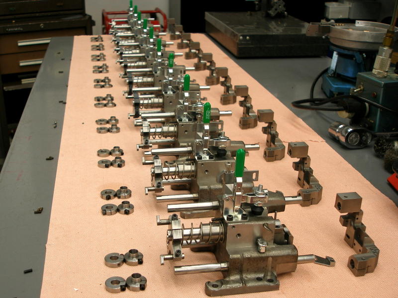 many metal parts with green handles laid out on a pink cloth on a workbench
