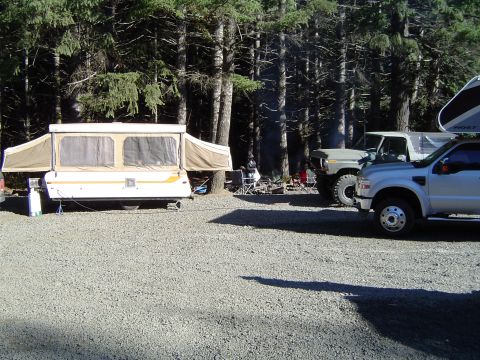 1978 Ford Bronco - A campsite scene features a silver pickup truck, a green SUV, and a pop-up camper set up among trees.