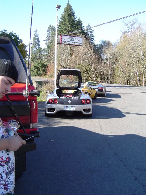1978 Ford Bronco - Three exotic sports cars are lined up on a sunny day near a gas station.
