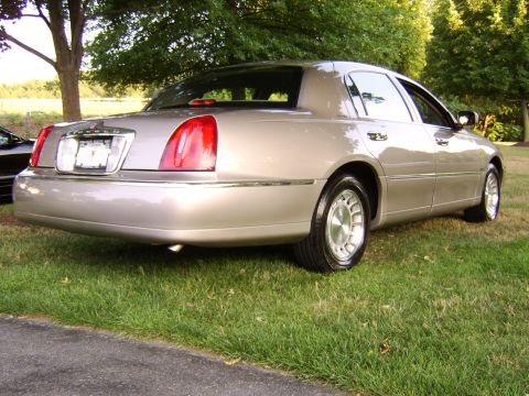 1996 Mercury Grand Marquis - This tan sedan features a classic design with chrome accents and prominent taillights, likely from the early 2000s.