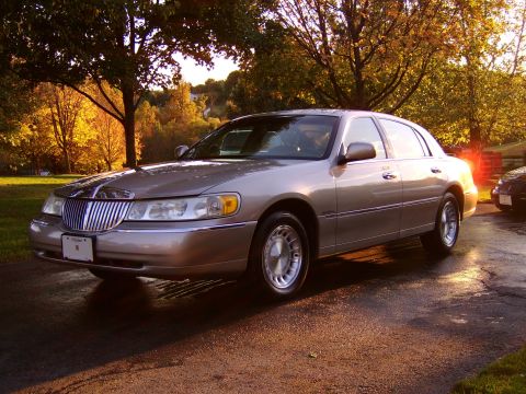 1996 Mercury Grand Marquis - A 1996 Mercury Grand Marquis sits on a wet driveway during golden hour, with fall foliage in the background.