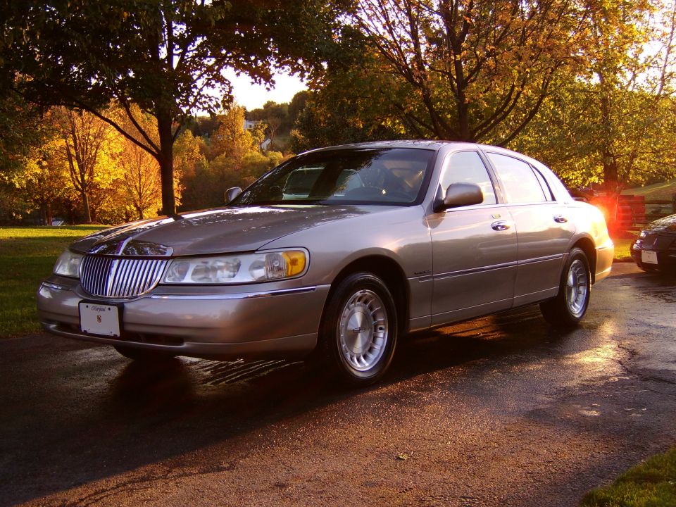 Silver Lincoln Town Car luxury sedan parked on driveway at sunset