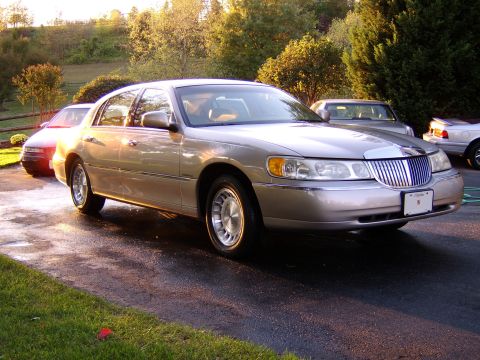 1996 Mercury Grand Marquis - A tan Lincoln Town Car is parked on a wet driveway with trees in the background.