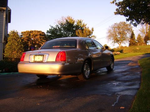 1996 Mercury Grand Marquis - A tan Lincoln Town Car is parked on a wet driveway during sunset.