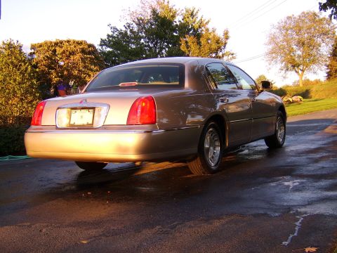 1996 Mercury Grand Marquis - This tan sedan, likely from the early 2000s, is shown from the rear in a 3/4 view.