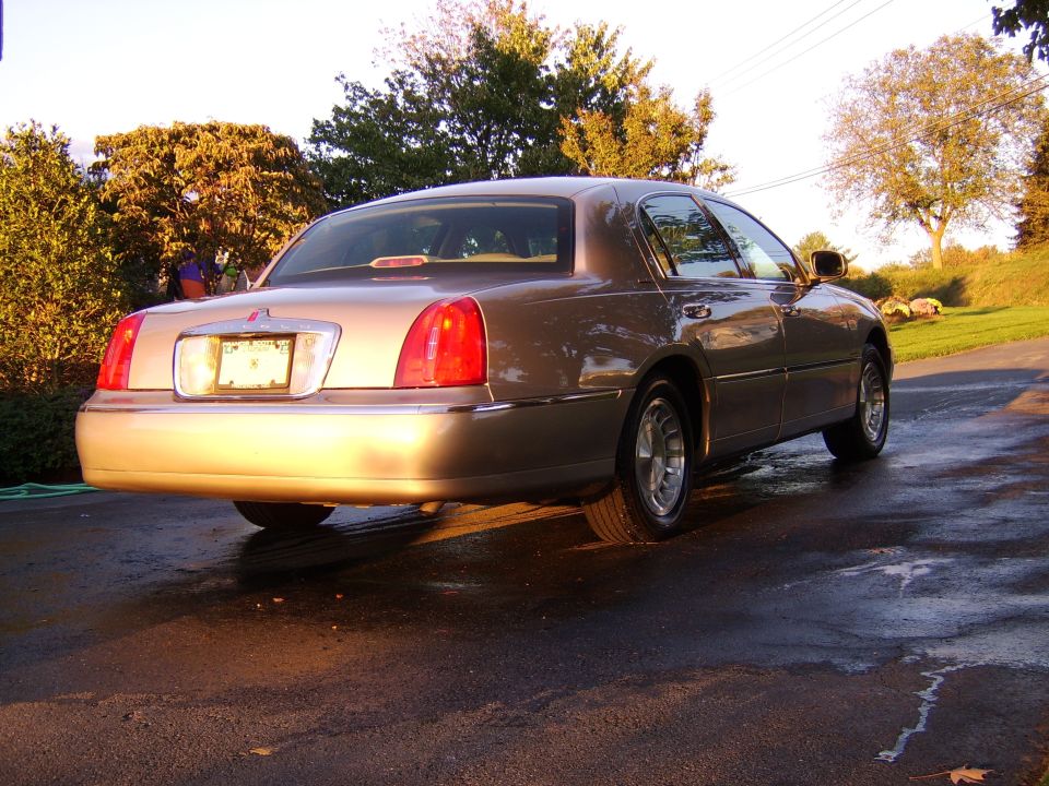 Gold Lincoln Town Car sedan, rear three-quarter view on wet driveway at golden hour
