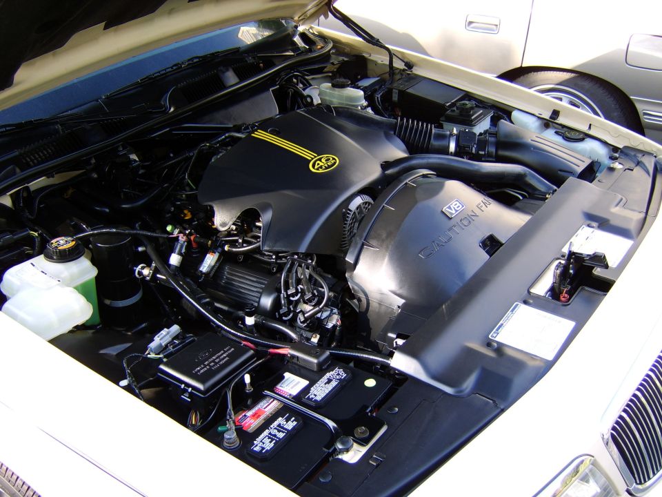V8 engine bay with black engine cover, yellow stripes, air box labeled CAUTION FAN, and battery.